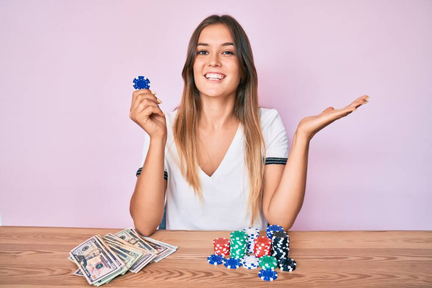 Красива біла жінка, граючи в покер, тримає фішки казино, святкуючи перемогу з щасливою посмішкою і виразом переможця з піднятими руками
  - Фото, зображення
