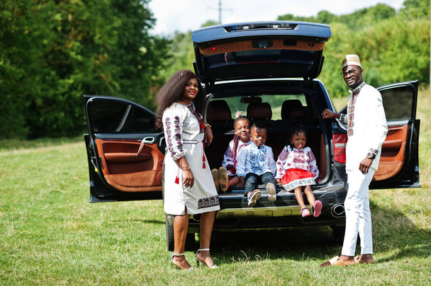 African family in traditional clothes stand against their car, kids sit on trunk. - Photo, image
