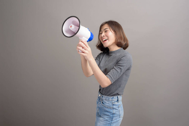 A portrait of young beautiful asian woman holding megaphone over studio background. - 写真・画像