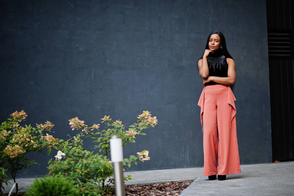 Fashionable african american woman in peach pants and black blouse pose outdoor. - Foto, Imagem