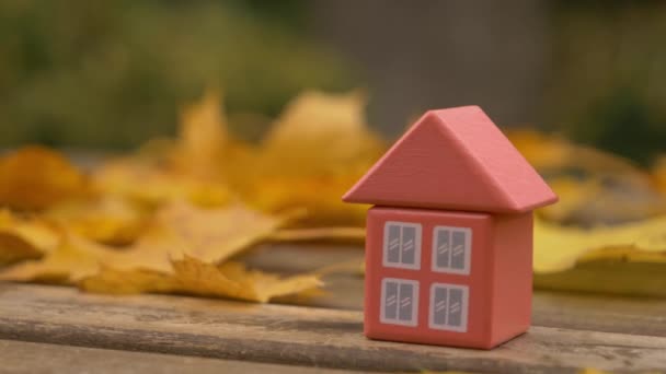 Piccola casa giocattolo accanto a foglie di autunno su un tavolo  - Filmati, video
