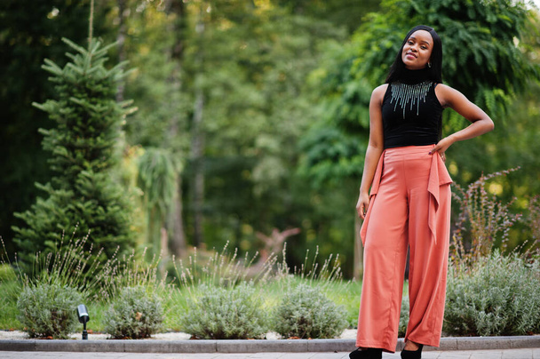 Fashionable african american woman in peach pants and black blouse pose outdoor. - Photo, image
