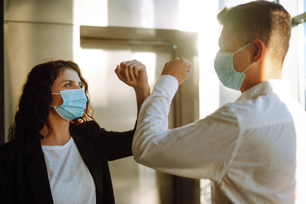Business colleagues in protective face masks bumping elbows while greeting each other near elevator at modern office. Covid-19. - Fotó, kép