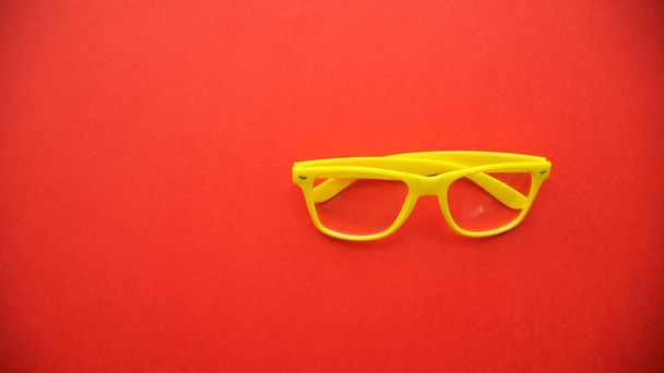 赤い背景をした黄色い眼鏡 - 写真・画像