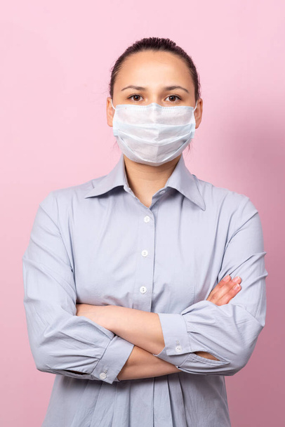 Portrait of young woman in mask looking at camera, on pink background. Flu epidemic, dust allergy, virus protection. City air pollution concept. - Foto, imagen