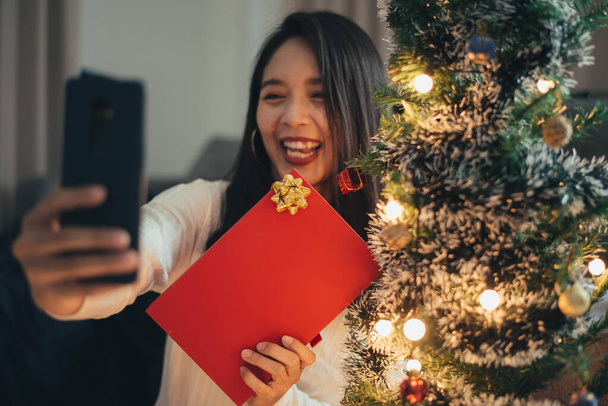 Woman making videocall her friends from home on Christmas day. Young smiling woman celebrating christmas with family and friends from smrtphone. - Photo, Image