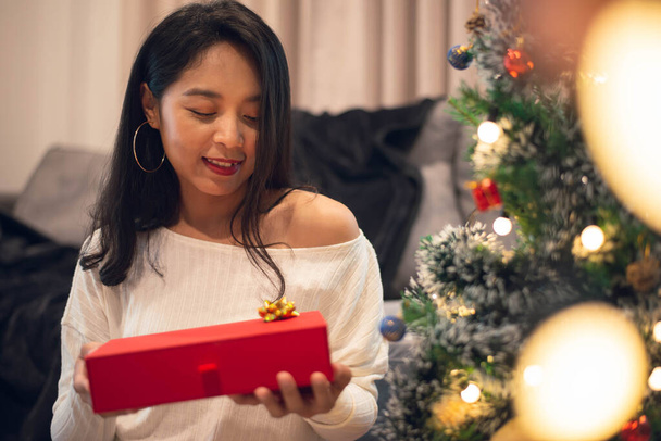 クリスマスの日に女性は驚きとクリスマスのギフトボックスを探しています。幸せな女の子とクリスマスプレゼントのために自宅でクリスマスを祝う. - 写真・画像