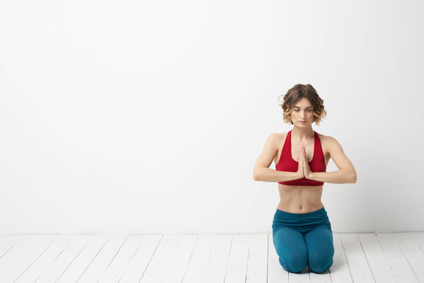Una donna in jeans blu pratica yoga su uno sfondo chiaro all'interno e una figura sottile in ginnastica - Foto, immagini