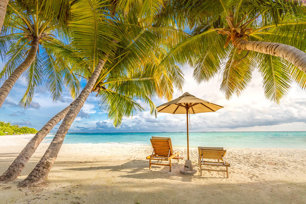 Piękny tropikalny zachód słońca, dwa leżaki, leżaki, parasol pod palmą. Biały piasek, widok na morze z horyzontem, kolorowe niebo zmierzch, spokój i relaks. Inspirujące hotel Beach Resort - Zdjęcie, obraz