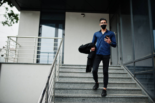 Middle eastern entrepreneur wear black face mask and eyeglasses look at mobile phone. New normal life after coronavirus pandemia. - Valokuva, kuva
