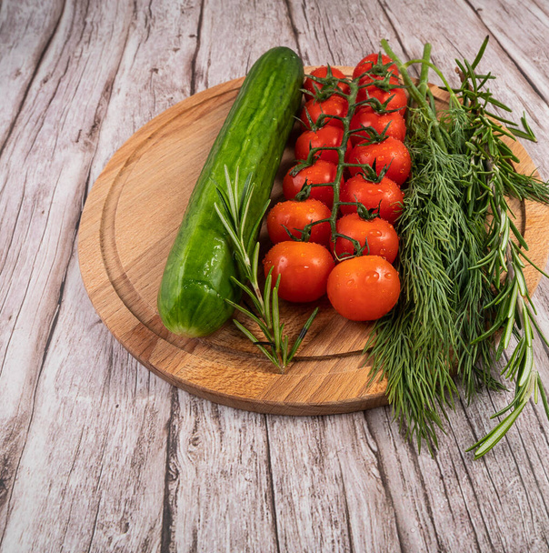 Washed vegetables for making salad.Cucumber, tomatoes, dill, rosemary on a wooden Board with water droplets. - Фото, зображення