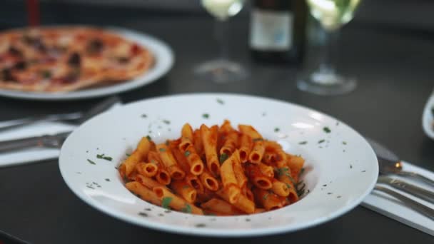 Gourmet-Pasta neben einer Pizza, zwei Weingläsern und einem Salat auf einem schwarzen Tisch - Filmmaterial, Video