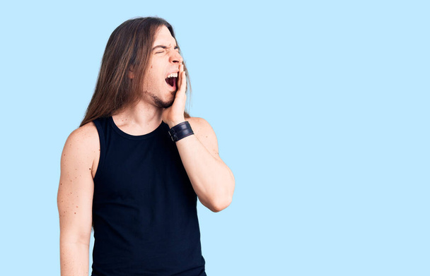 Young adult man with long hair wearing goth style with black clothes bored yawning tired covering mouth with hand. restless and sleepiness.  - Photo, Image