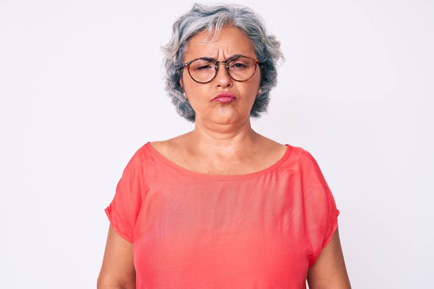 シニアヒスパニック系の白髪の女性がカジュアルな服や眼鏡を着用落ち込んで苦痛のために心配し、怒っていると恐れて泣いている。悲しい表情.  - 写真・画像