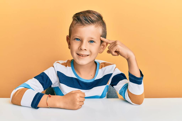 Adorable caucasian kid wearing casual clothes sitting on the table smiling pointing to head with one finger, great idea or thought, good memory  - Foto, immagini