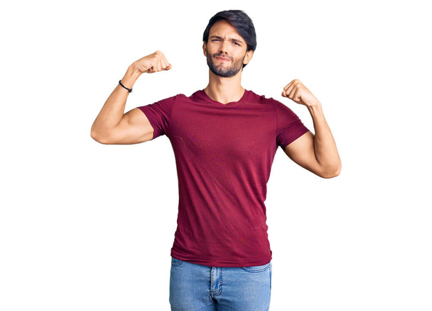 Hombre hispano guapo usando ropa casual mostrando los músculos de los brazos sonriendo orgulloso. concepto de fitness.  - Foto, imagen