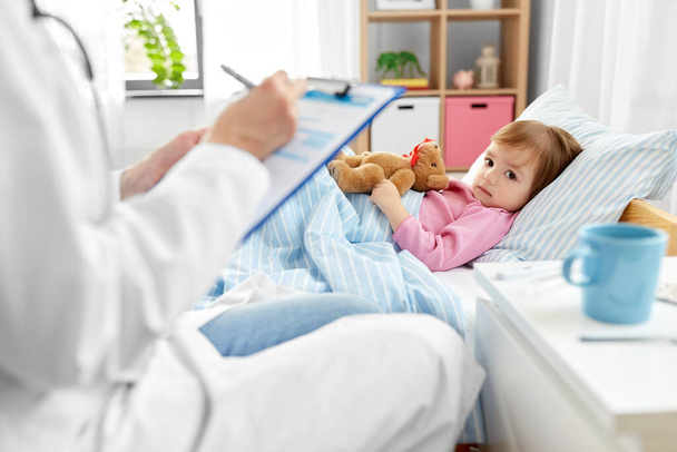 Arzt mit Klemmbrett und krankes Mädchen zu Hause im Bett - Foto, Bild