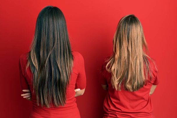 Hispanic family of mother and daughter wearing casual clothes over red background standing backwards looking away with crossed arms  - Foto, immagini