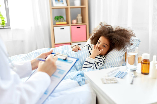 doctor with clipboard and sick girl in bed at home - Foto, Imagen