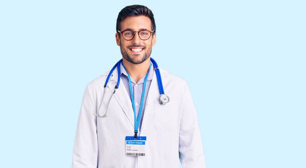 Young hispanic man wearing doctor uniform and stethoscope with a happy and cool smile on face. lucky person.  - Valokuva, kuva