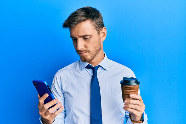 Handsome caucasian business man using smartphone and drinking a cup of coffee relaxed with serious expression on face. simple and natural looking at the camera.  - Фото, зображення