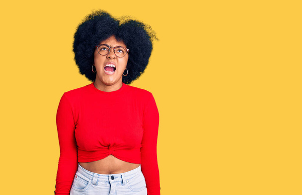 Genç Afro-Amerikalı kız günlük kıyafetler ve gözlük takıyor kızgın ve kızgın çığlık atıyor sinirli ve öfkeli, öfkeyle bağırıyor. öfke ve agresif konsept.  - Fotoğraf, Görsel