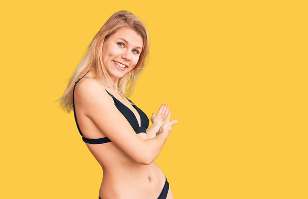 jong mooi blond vrouw dragen bikini uitnodigen naar binnen glimlachen natuurlijk met open hand  - Foto, afbeelding