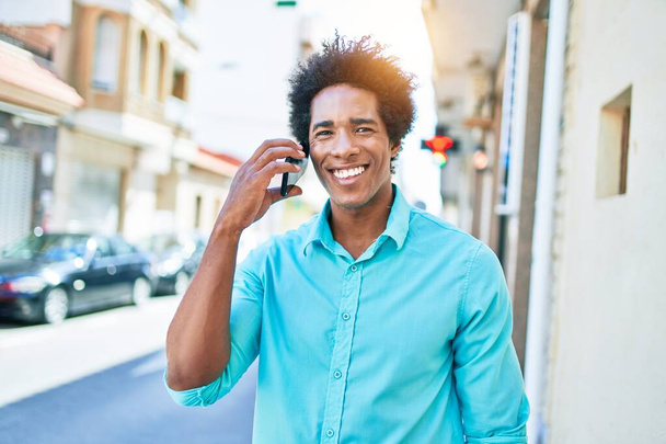 Young handsome african american man wearing casual clothes smiling happy. Standing with smile on face having conversation talking on the smartphone at town street. - Photo, Image