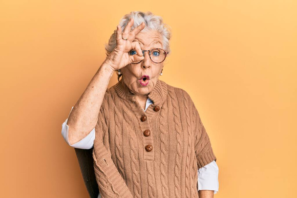 Femme âgée aux cheveux gris portant des vêtements décontractés et des lunettes faisant un geste correct choqué par le visage surpris, les yeux regardant à travers les doigts. expression incrédule.  - Photo, image