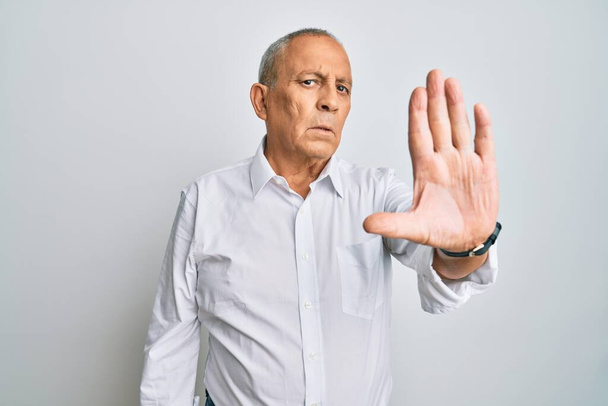 Pohledný starší muž v neformální bílé košili přestane zpívat dlaní. varovný výraz s negativním a vážným gestem na tváři.  - Fotografie, Obrázek