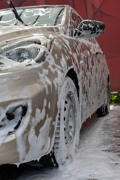 Beige επιβατικό αυτοκίνητο σε αφρό σαμπουάν close-up αριστερή πλευρά κάθετη φωτογραφία, υπηρεσία πλυντηρίου αυτοκινήτων, φροντίδα του οχήματος - Φωτογραφία, εικόνα