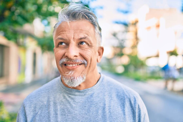 Der grauhaarige Mann mittleren Alters lächelt glücklich in der Stadt.  - Foto, Bild