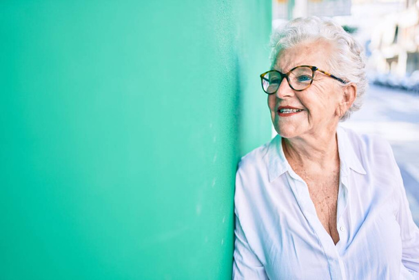 Ältere Seniorin mit grauen Haaren lächelt glücklich an die Wand gelehnt - Foto, Bild