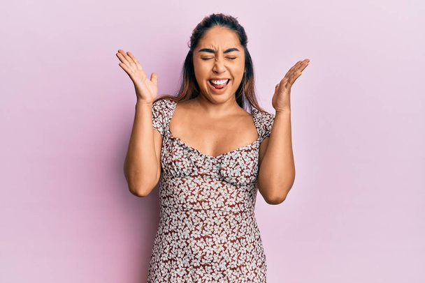 Νεαρή Λατίνα γυναίκα φορώντας casual ρούχα γιορτάζει τρελός και τρελός για την επιτυχία με τα χέρια ψηλά και κλειστά μάτια ουρλιάζοντας ενθουσιασμένος. έννοια νικητή  - Φωτογραφία, εικόνα
