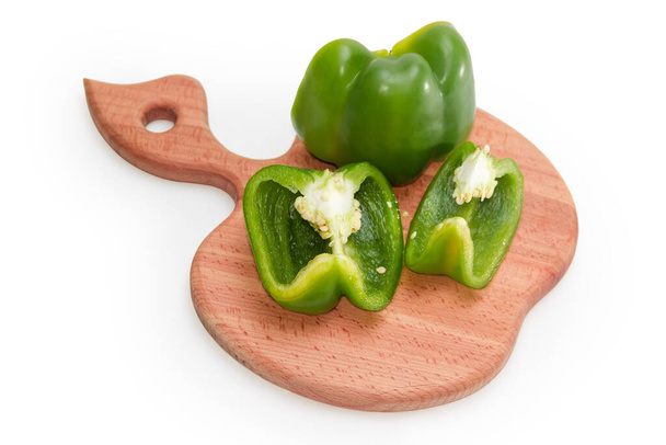 Οι μισές φέτες πράσινου πιπεριού με σπόρους βρίσκονται στο ξύλο κοπής σε σχήμα μήλου σε λευκό φόντο, επιλεκτική εστίαση - Φωτογραφία, εικόνα