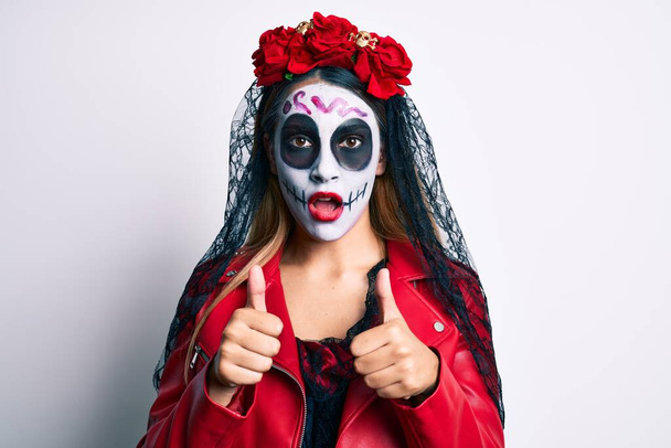 Vrouw draagt dag van het dode kostuum met duimen omhoog doet ok teken in shock gezicht, op zoek sceptisch en sarcastisch, verrast met open mond  - Foto, afbeelding