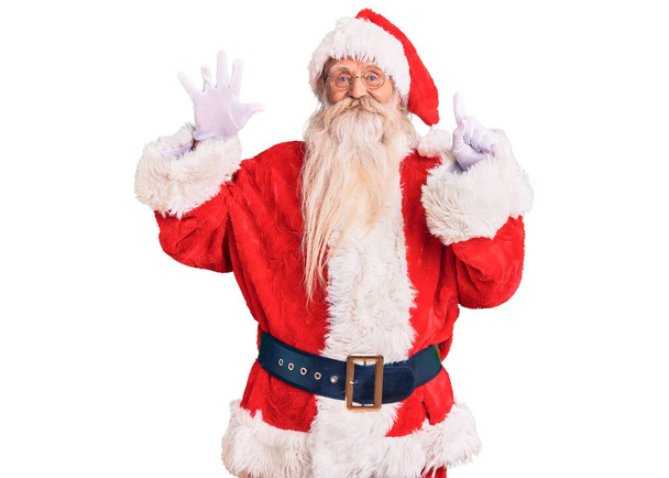 Viejo hombre mayor con el pelo gris y la barba larga con traje tradicional de Santa Claus mostrando y señalando hacia arriba con los dedos número seis mientras sonríe confiado y feliz.  - Foto, imagen