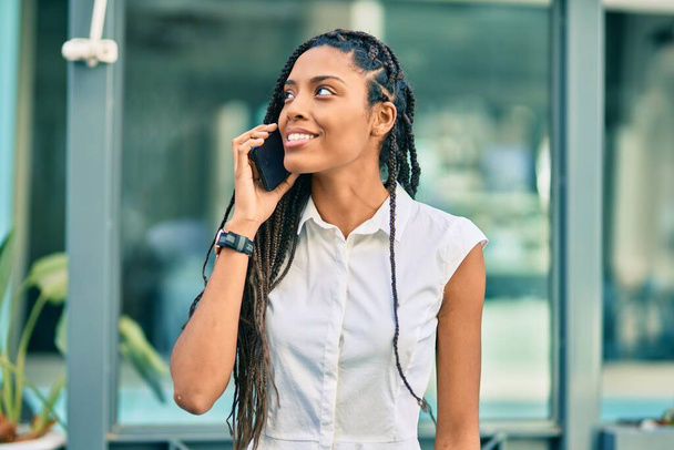 Joven mujer afroamericana sonriendo feliz hablando en el teléfono inteligente en la ciudad. - Foto, Imagen