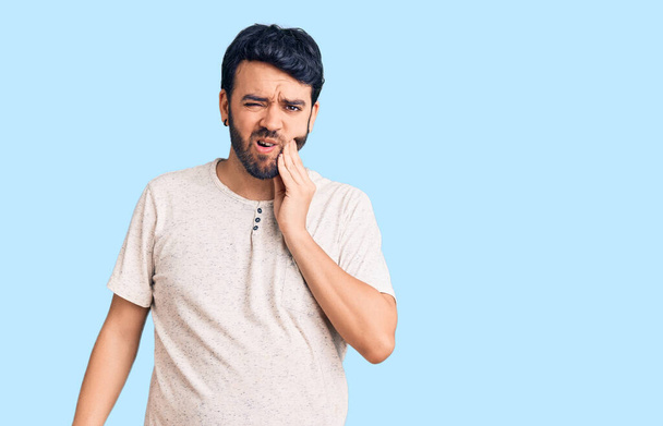 Young hispanic man wearing casual clothes touching mouth with hand with painful expression because of toothache or dental illness on teeth. dentist  - 写真・画像