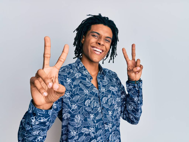 Mladý africký Američan v tričku ve stylu 80. let, usmívá se a dívá se na kameru ukazující prsty ukazující znamení vítězství. číslo dvě.  - Fotografie, Obrázek