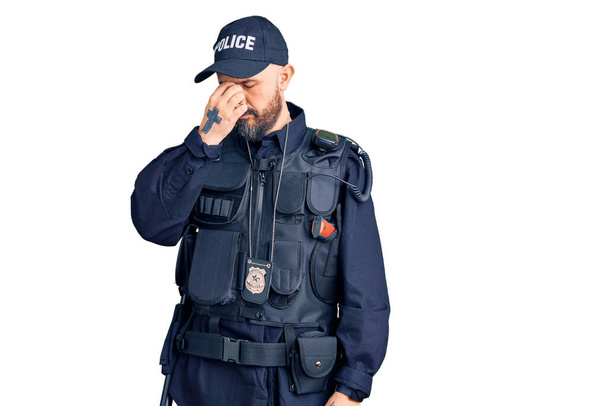 Ein junger gutaussehender Mann in Polizeiuniform reibt sich müde Nase und Augen und spürt Müdigkeit und Kopfschmerzen. Konzept für Stress und Frustration.  - Foto, Bild