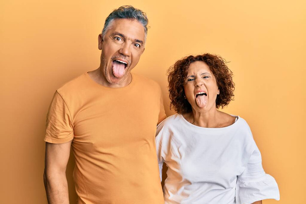 Beautiful middle age couple together wearing casual clothes sticking tongue out happy with funny expression. emotion concept.  - Photo, Image