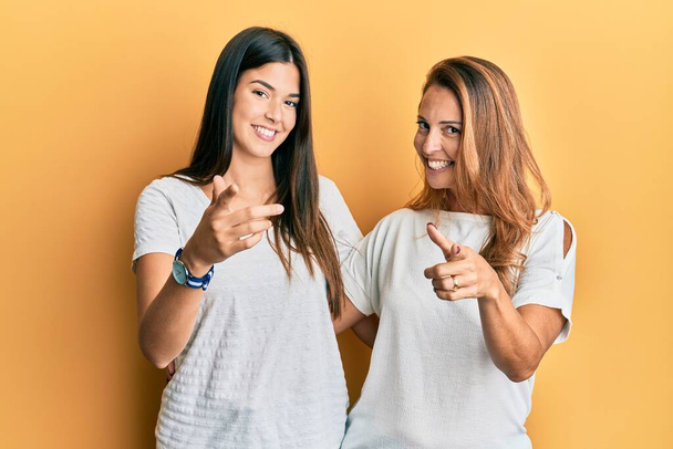 Família hispânica de mãe e filha vestindo camiseta branca casual apontando os dedos para a câmera com rosto feliz e engraçado. boa energia e vibrações.  - Foto, Imagem