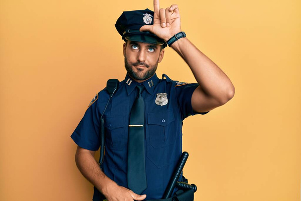 bel homme hispanique portant l'uniforme de la police se moquant des gens avec les doigts sur le front faisant geste perdant moqueur et insultant.  - Photo, image