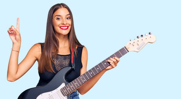 若いですヒスパニック女性遊びます電気ギター驚きでアイデアや質問を指差す指で幸せな顔,ナンバーワン  - 写真・画像