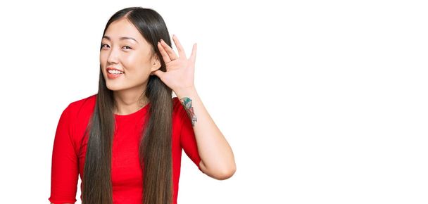 Young chinese woman wearing casual clothes smiling with hand over ear listening an hearing to rumor or gossip. deafness concept.  - Фото, изображение
