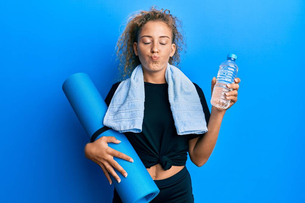 Beautiful caucasian teenager girl holding yoga mat and water bottle looking at the camera blowing a kiss being lovely and sexy. love expression.  - Valokuva, kuva