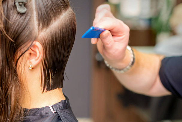 Vista lateral de la mano de peluquero haciendo corte de pelo de mujer joven por peine en peluquería - Foto, Imagen