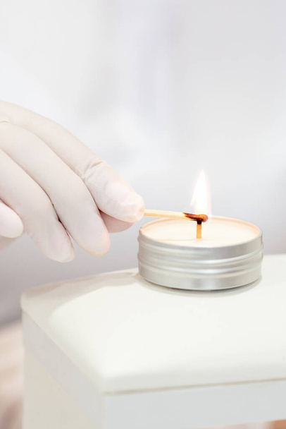 Мастер маникюра в белых перчатках зажигает свечу спичкой в маникюре - Фото, изображение