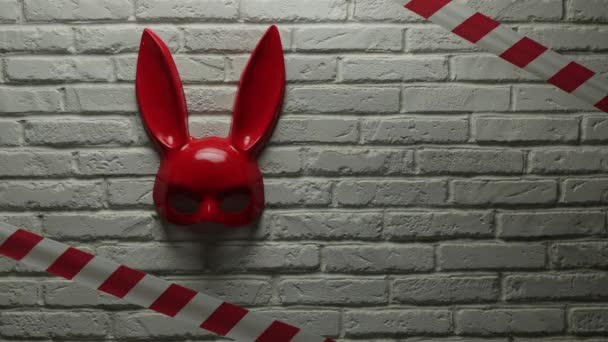 red rabbit mask on a white brick texture wall and red and white signal tape - Footage, Video